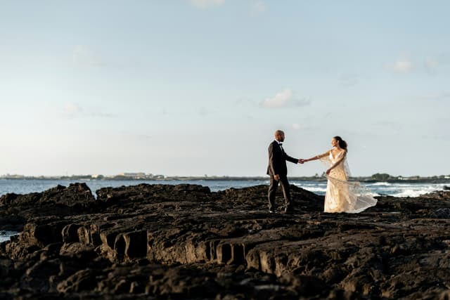 Couple holding hands on a rocky shoreline at sunset in Hawaii